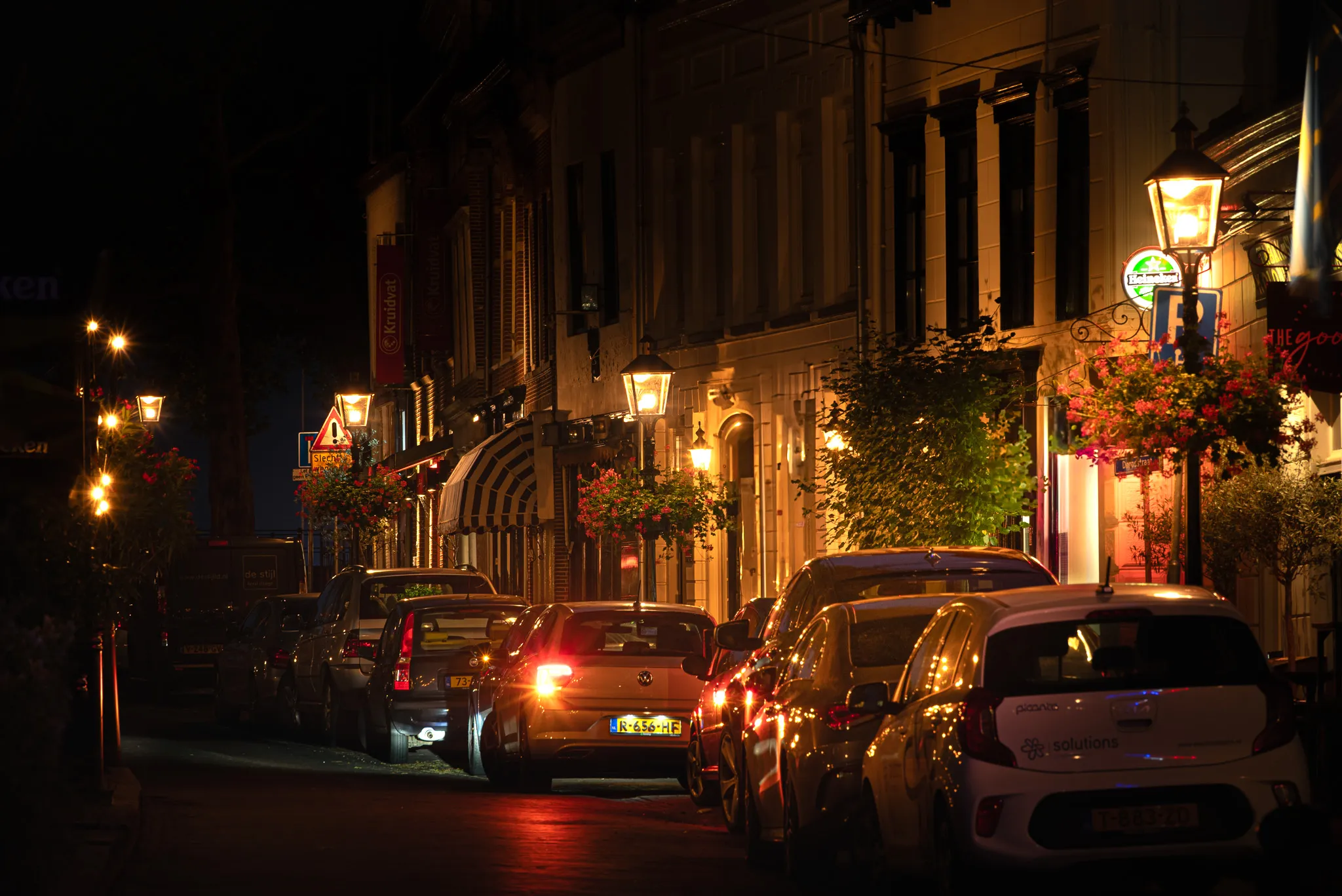 Een nachtelijke foto van een straat met auto's verlicht door klassieke buitenverlichting
